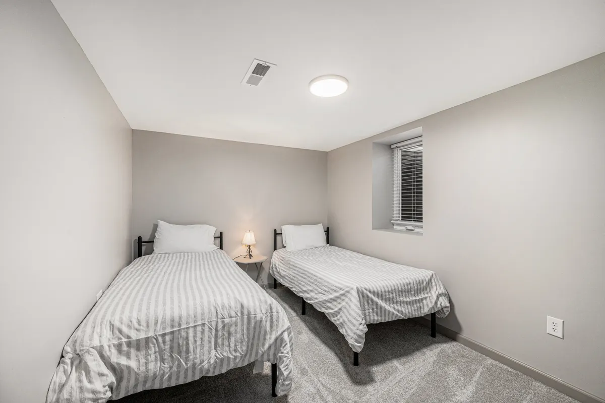 A peaceful bedroom with two single beds, a nightstand with a glowing lamp, and natural light from a nearby window. The room feels inviting and versatile, ideal for families or friends traveling together.