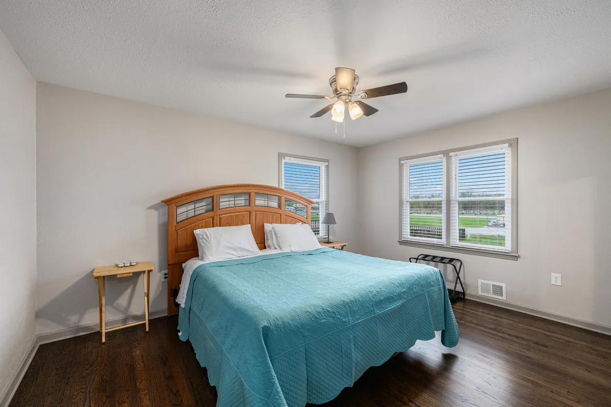 A sunlit bedroom with a sturdy wooden bed frame, turquoise bedspread, and large windows. The space is bathed in natural light, creating a welcoming environment for relaxation, reading, or enjoying a hot beverage in the morning.