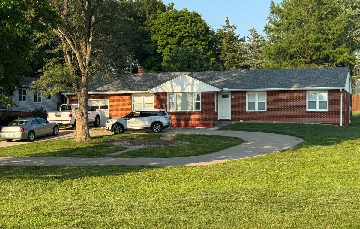 This exterior image showcases the red brick facade of Bridge Street B&B surrounded by a lush front yard, a curved driveway, and large trees. The scene is lively and welcoming, with children playing games on the well-kept lawn and families gathering outdoors, suggesting a sense of community and togetherness.