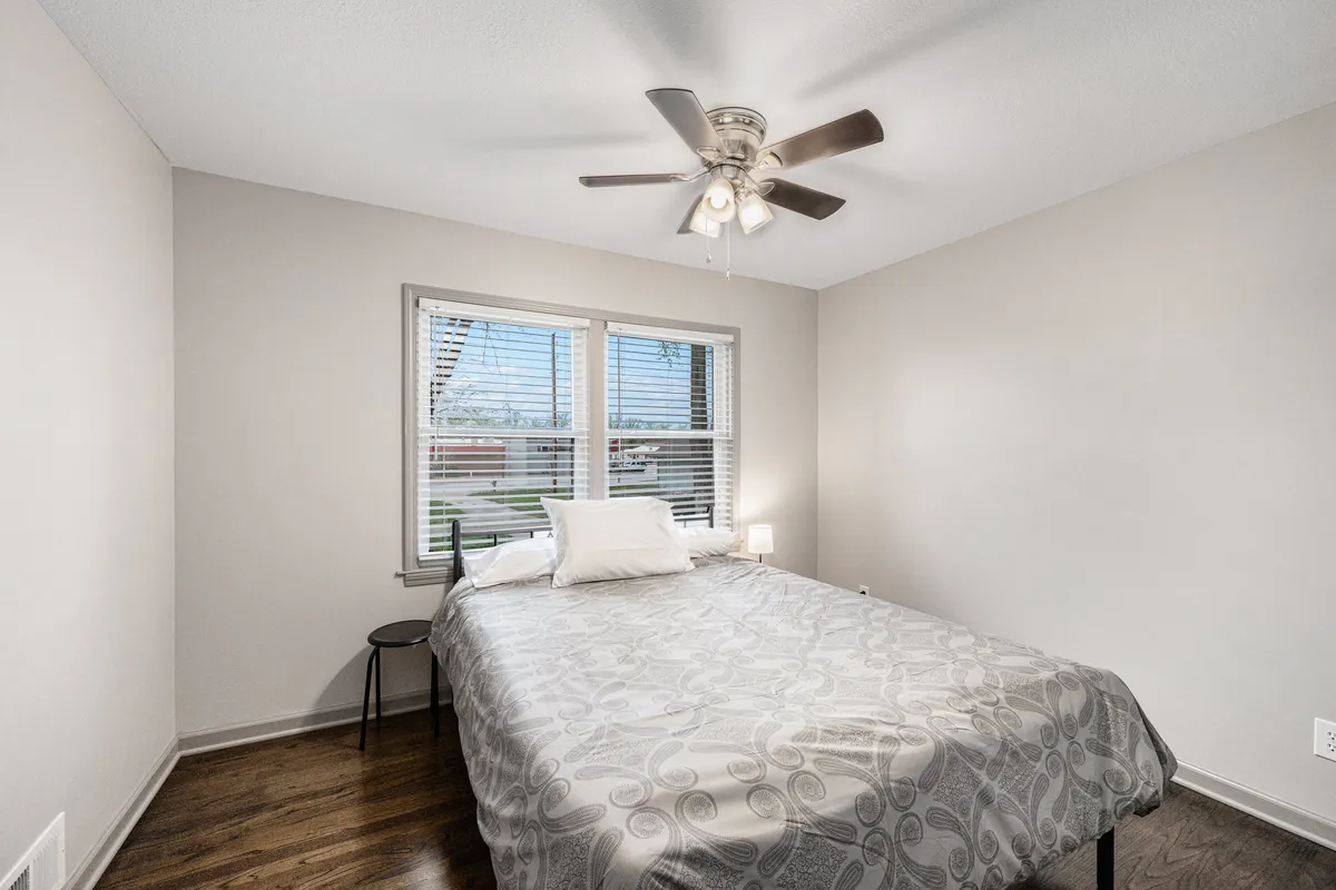 A serene bedroom featuring a comfortable bed, window, and ceiling fan. Soft lighting and a tranquil mood encourage restful reading or meditation, embodying a quiet escape where classic hospitality meets modern comfort.