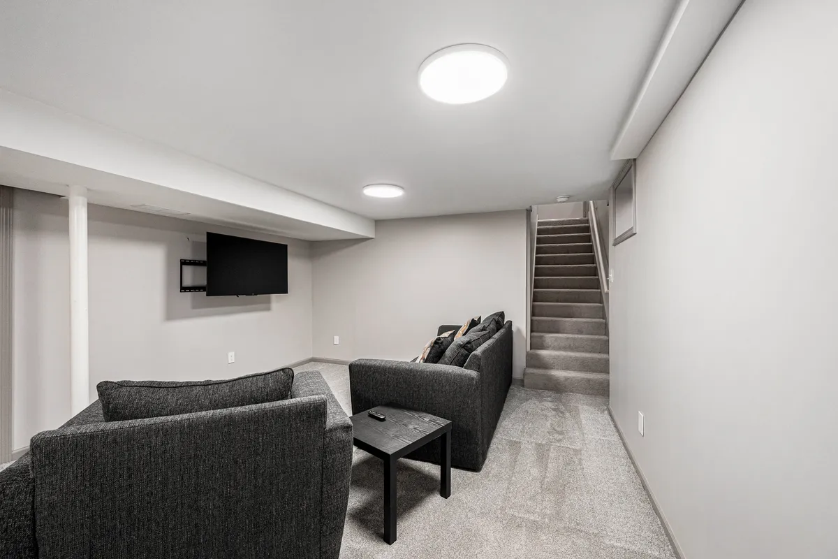 A casual living space featuring a sofa set, coffee table, television, and a visible staircase. The area is designed for relaxation and socializing, with a layout that encourages group interaction—perfect for movie nights or intimate gatherings. Warm, ambient lighting and practical furnishings contribute to a welcoming vibe.